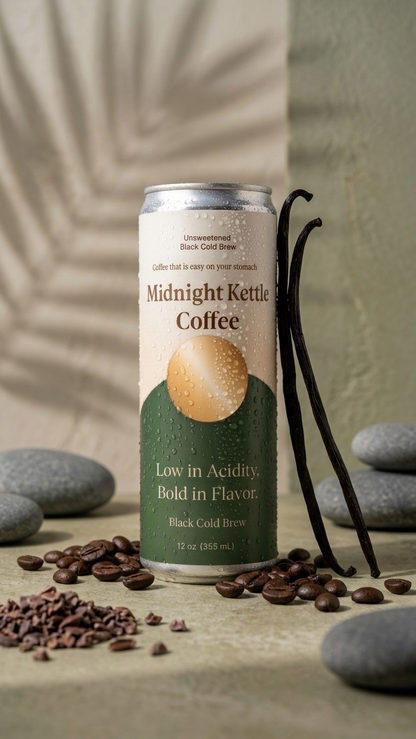 A 12 oz can of Midnight Kettle Coffee, Black Cold Brew, standing on a textured stone surface with coffee beans, vanilla beans, and smooth stones. The background is a soft beige fabric drape.